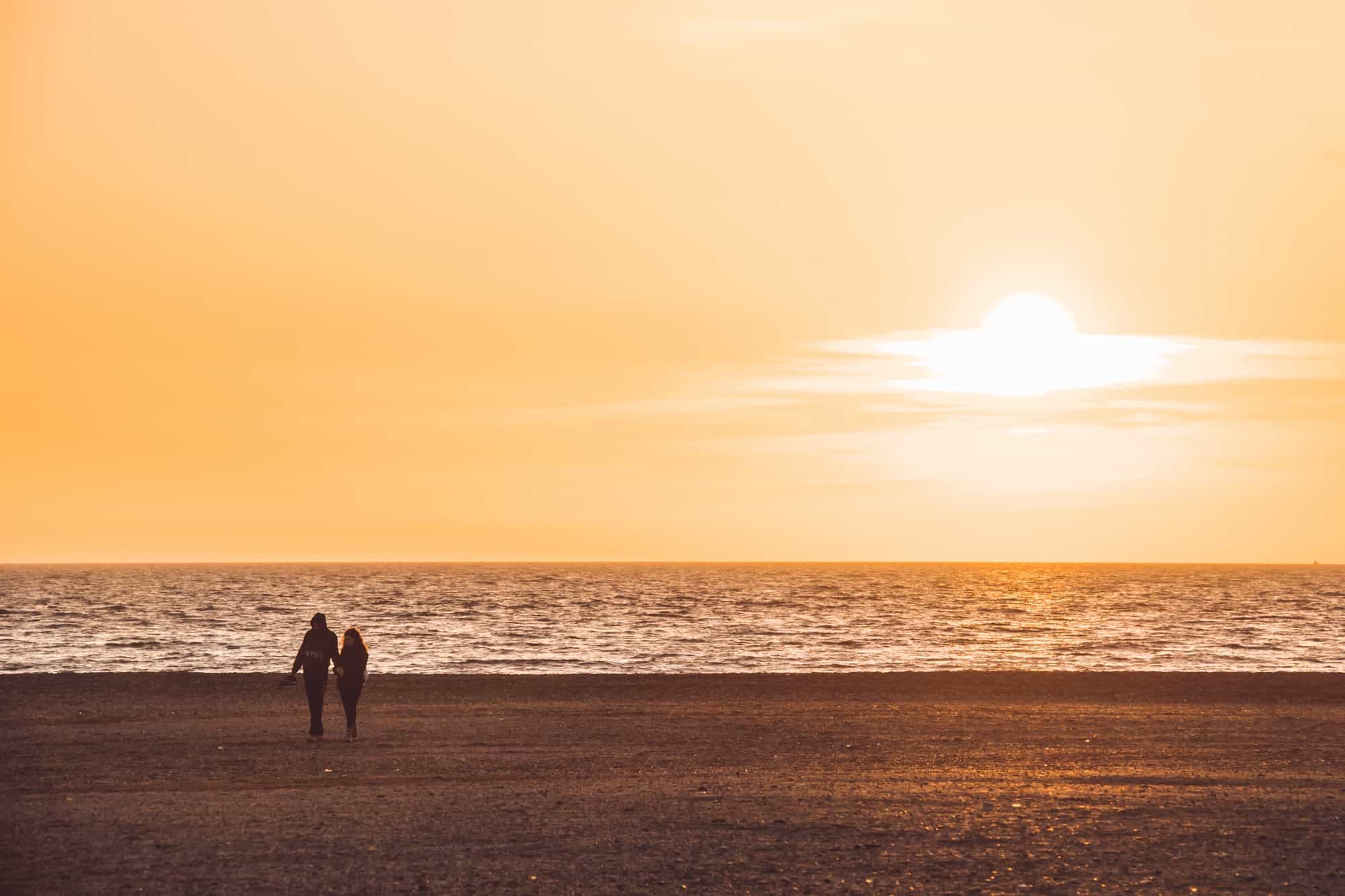 silhouette of couple walking on the beach on orange sunset background, almerimar, almeria, spain